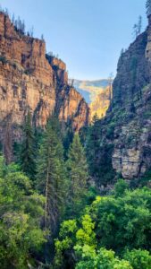 Sunlit canyon walls rise high above the trail to Hanging Lake, with golden morning light highlighting the rugged rock formations.
