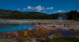 A vibrant, colorful geyser bubbles in Biscuit Basin, Yellowstone, displaying stunning shades of orange, yellow, and blue in the park's geothermal landscape.
